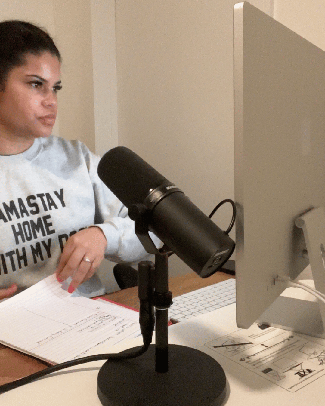 Jordan Gill at her desk with a Mac, microphone, and notebook under warm light